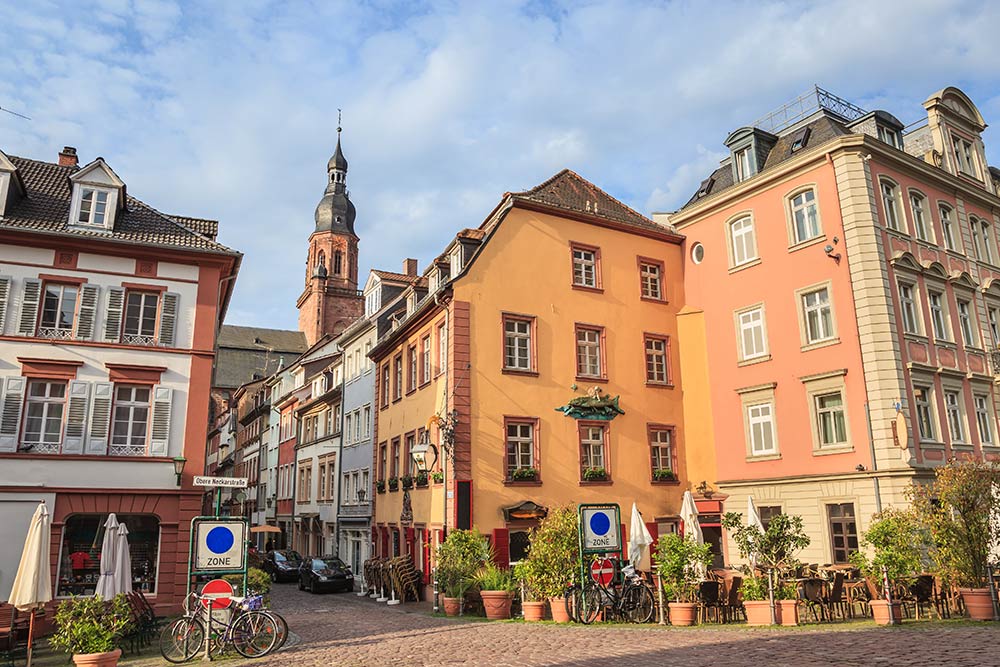 Blick in die Heidelberger Steingasse, einer kleinen Gasse gesäumt von bunten Häusern mit Heiliggeistkirche im Hintergrund